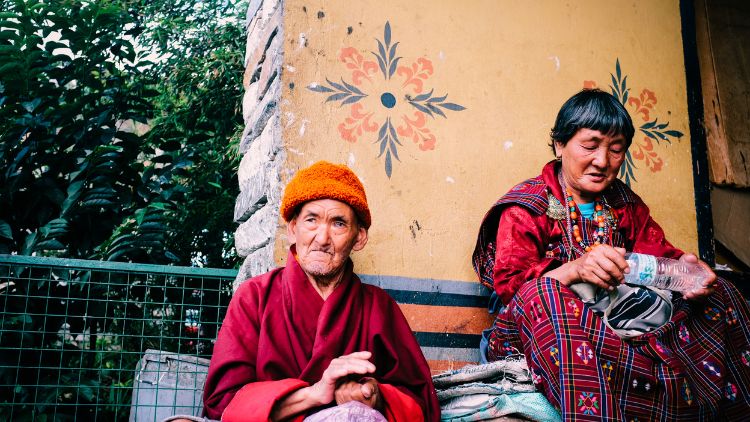 A man in Red Robe Sitting beside a Green Metal Fence