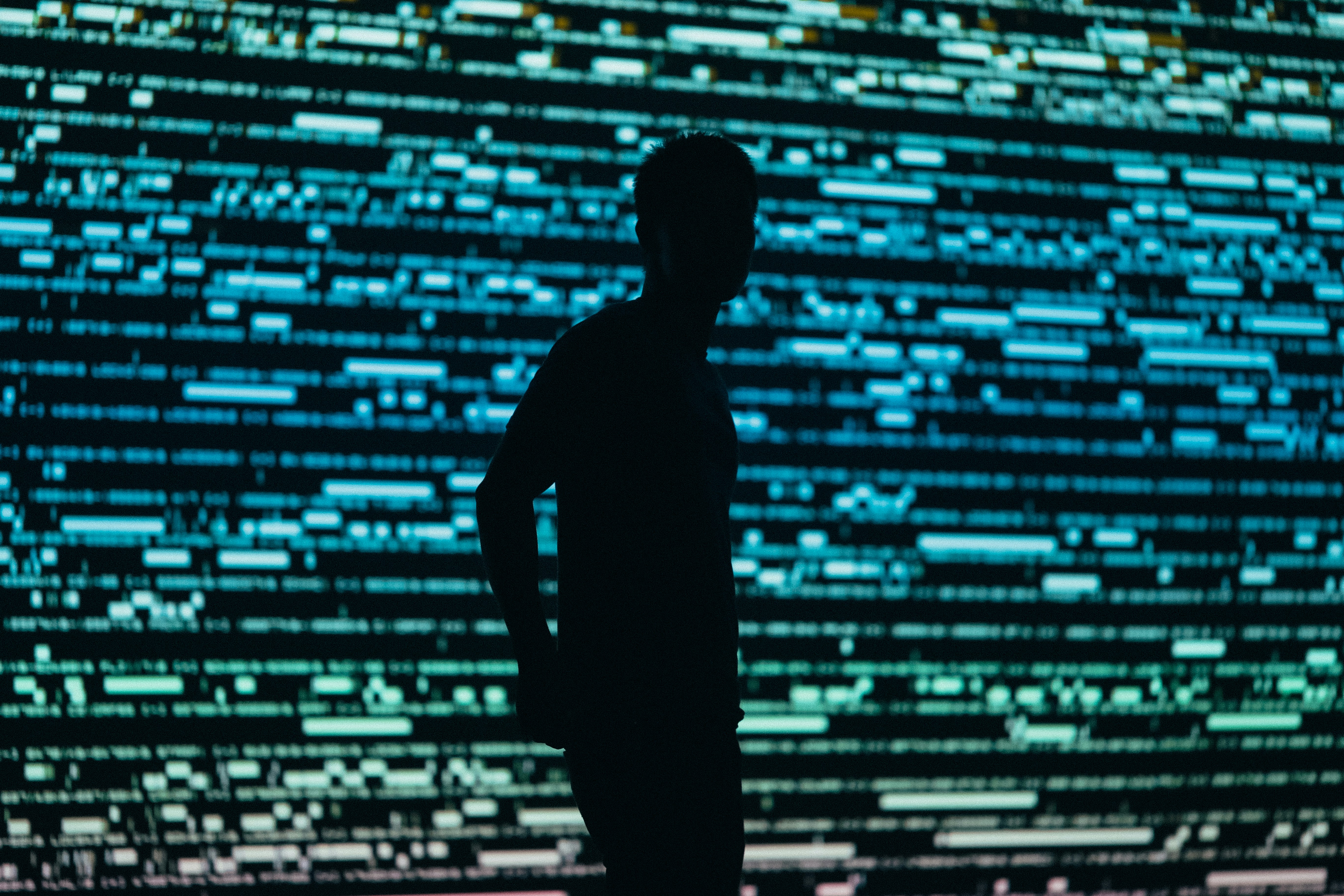 Dark silhouette of a person in front of a big screen full of gree and blue data