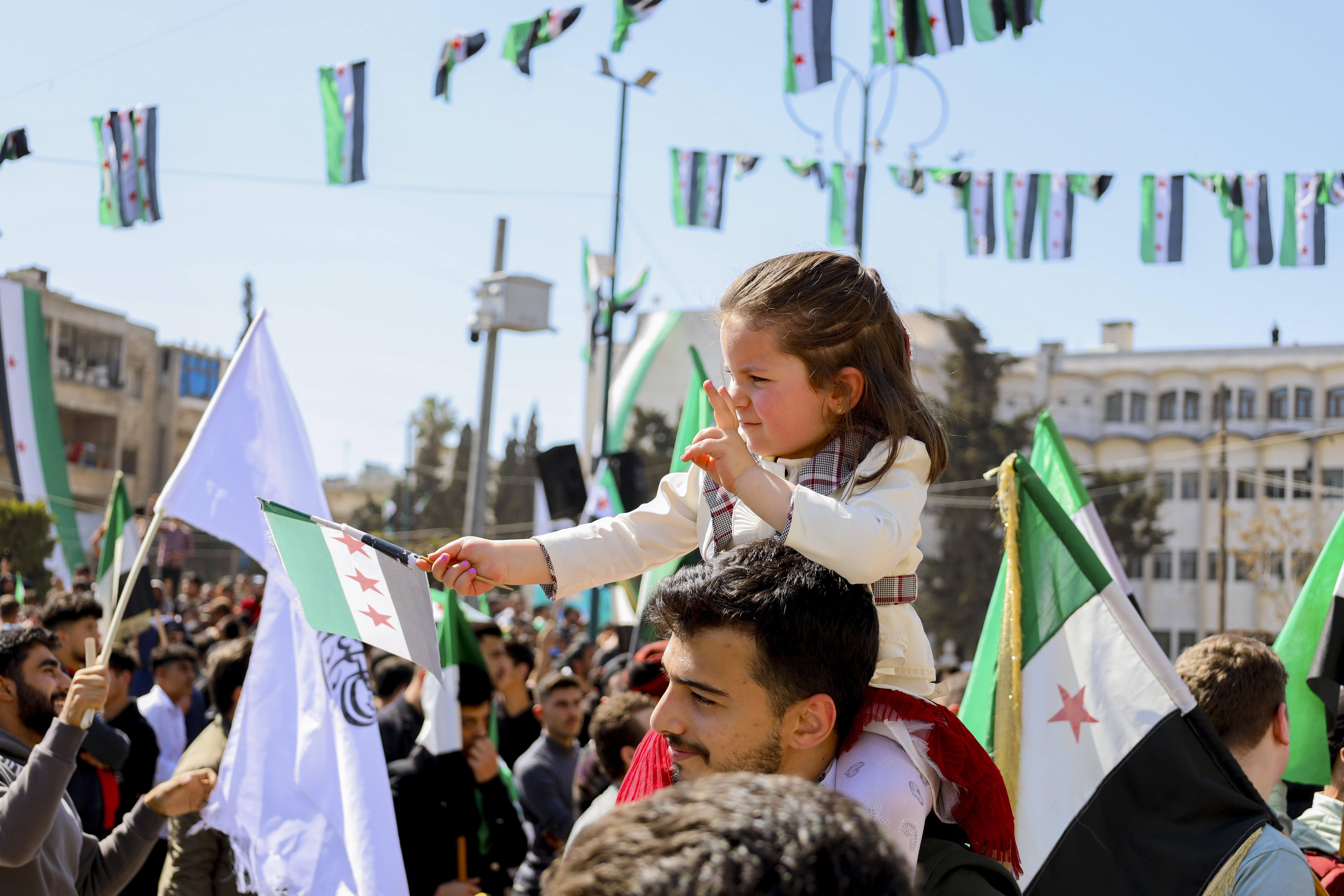 Ein Mädchen sitzt auf den Schultern eines Mannes und schwenkt eine syrische Oppositionsflagge während einer Kundgebung in Idlib, Syrien, 