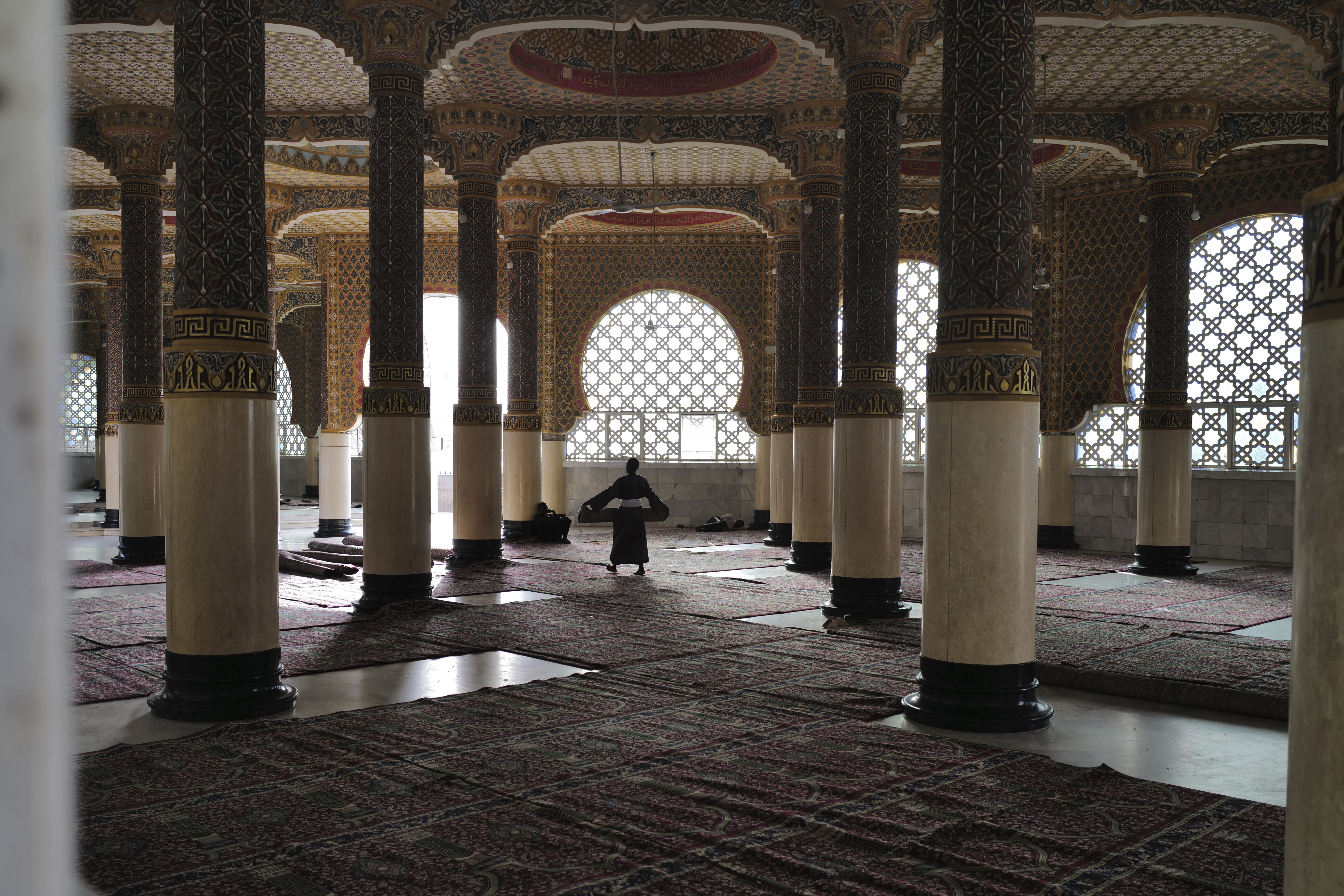 Ein Mann trägt einen Teppich in einem Gebetsraum in der Großen Moschee in Touba, Senegal,