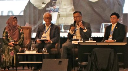 The first panel of the conference "Political Outlook". Four pictures are seen sitting in single chairs in front of a big screen on a stage. They are Aira Azhari (Moderator), Ibrahim Suffian (Panelist), Ooi Kok Hin (Panelist), Datuk Dr. Johan Arriffin Samad (Panelist).