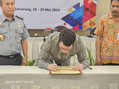 Dr. Stefan Diederich signing the Annual Work Plan document with Hantor Situmorang and Agung Kristianto seen standing on either side of him.