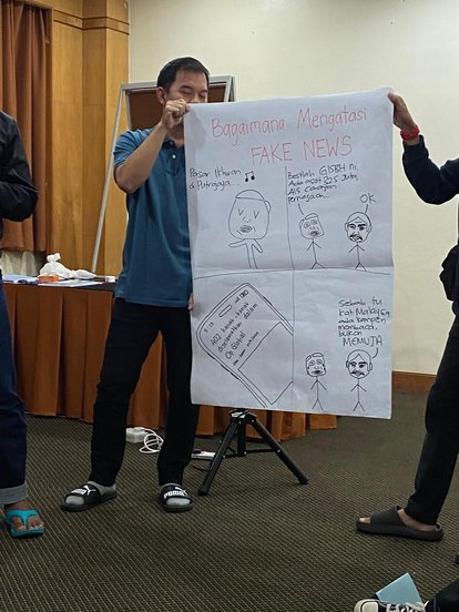 Two participants presenting the result of their brainstorming session. The paper they are holding shows a four panel comic titled, "How to Counter Fake News"