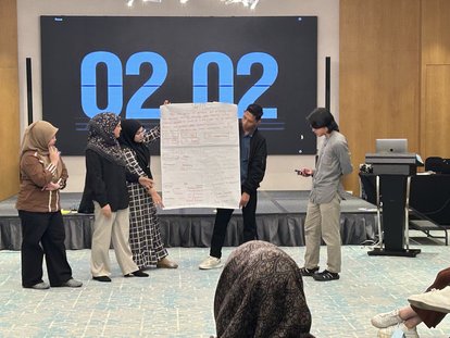 A group is presenting their ideas to the rest of the participants. Behind them, a digital timer was counting down their allocated time.