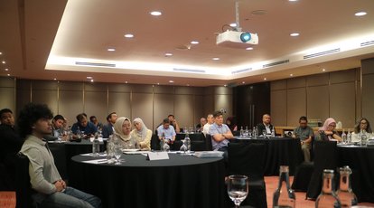 Participants of the talk are seen sitting in several round tables. Most were looking to the front where Dr. Diederich delivered his presentation, some were taking notes.