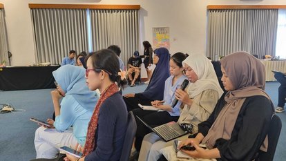 Seorang peserta, duduk di antara beberapa peserta lain, berpartisipasi dalam sesi diskusi. 