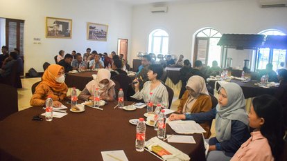 Sejumlah peserta duduk di sebuah meja bundar. Salah satu di antara mereka sedang memegang mic dan berbicara.