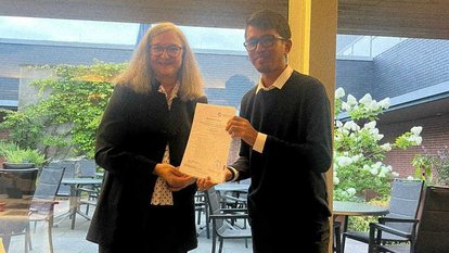 Rahman Imuda standing besides someone from Gummersbach. Both of them hold onto a piece of paper that looks like a certificate.