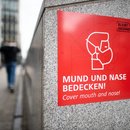Ein Schild mit einem Piktogramm und dem Aufdruck "Mund und Nase bedecken" weist auf das Tragen von Schutzmasken hin. 