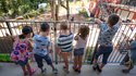 KInder stehen am Geländer und schauen in den Garten einer Kindertagesstätte 
