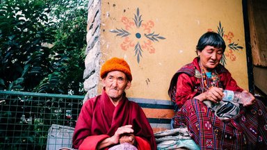 A man in Red Robe Sitting beside a Green Metal Fence