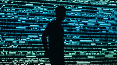Dark silhouette of a person in front of a big screen full of gree and blue data