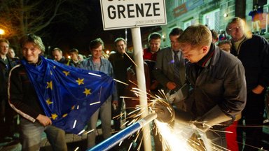 A worker removes the remains of an iron border fence dating back to the times of the Cold War at the German-Czech border in Bayerisch Eisenstein, southern Germany, Saturday, May 1, 2004, while a crowd of German and Czech people celebrates the expansion of the European Union at midnight.