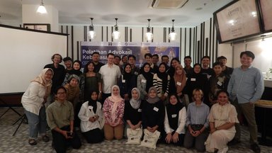 Participants of the event standing alongside Dr. Stefan Diederich, Project Director of FNF Indonesia, in front of a banner showing the event's details.