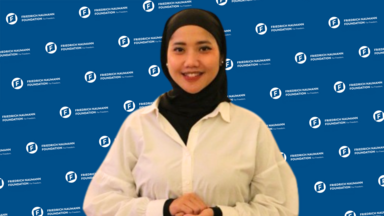 A photo of Nurul Fitriani with FNF background in blue. She wears white shirt and black hijab.
