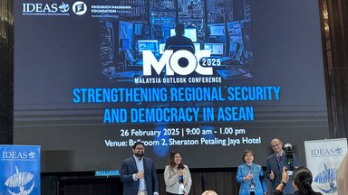 A picture from the stage of Malaysia Outlook Conference 2025. Four people (3 panelists and 1 moderator) are posing for a picture in front of the event banner.